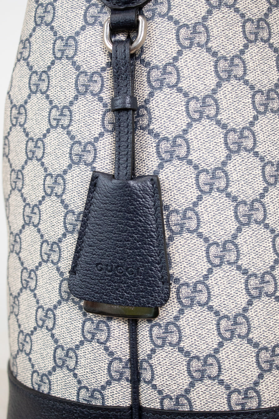 Close-up of 'GUCCI' bag charm detail shown against a GG monogrammed background