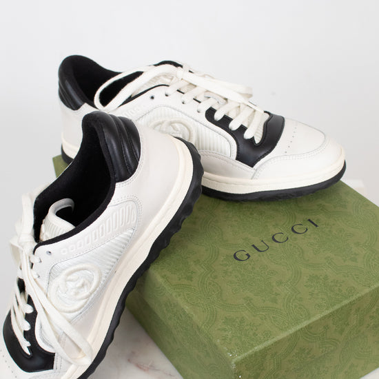 White and navy sneakers set on top of green 'GUCCI' box and laying against a plain background