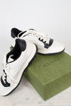 White and navy sneakers set on top of green 'GUCCI' box and laying against a plain background