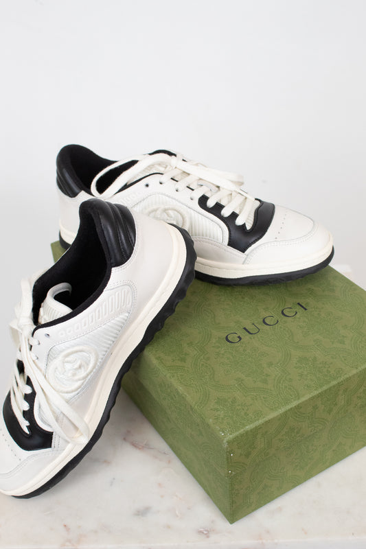 White and navy sneakers set on top of green 'GUCCI' box and laying against a plain background