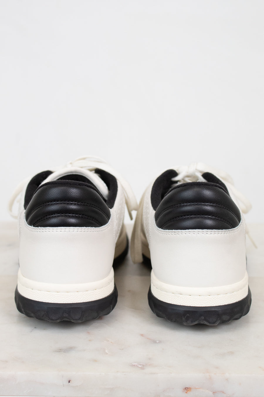 Heel view of white and navy sneakers against a plain marble background