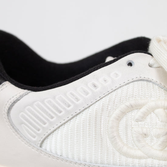 Close-up of canvas and leather white and navy sneakers showing canvas 'GG' embroidered side panel against a plain background