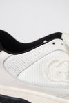 Close-up of canvas and leather white and navy sneakers showing canvas 'GG' embroidered side panel against a plain background