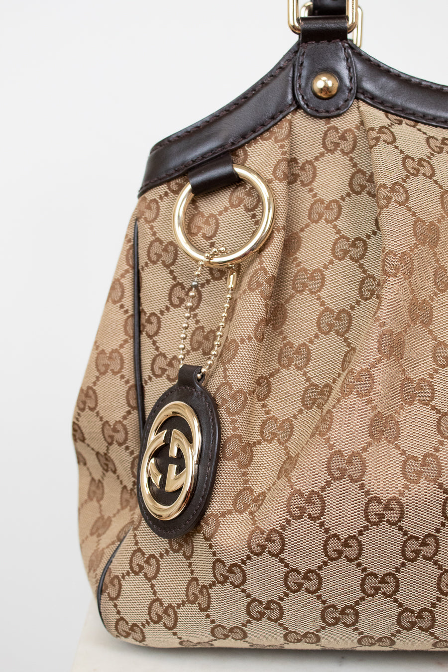 Close-up of a Gucci handbag with monogram pattern and keychain.