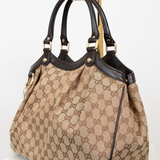 Beige handbag with brown Gucci monogram with brown handles on a white background