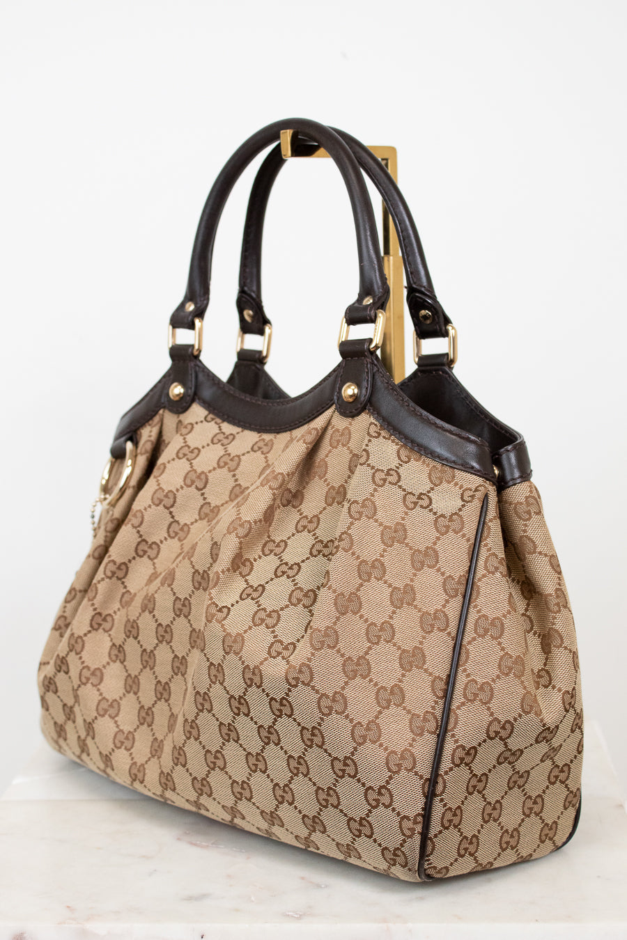 Beige handbag with brown Gucci monogram with brown handles on a white background
