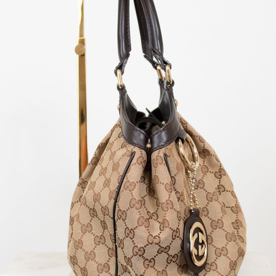 Side view of beige handbag with brown Gucci monogram with brown handles on a white background