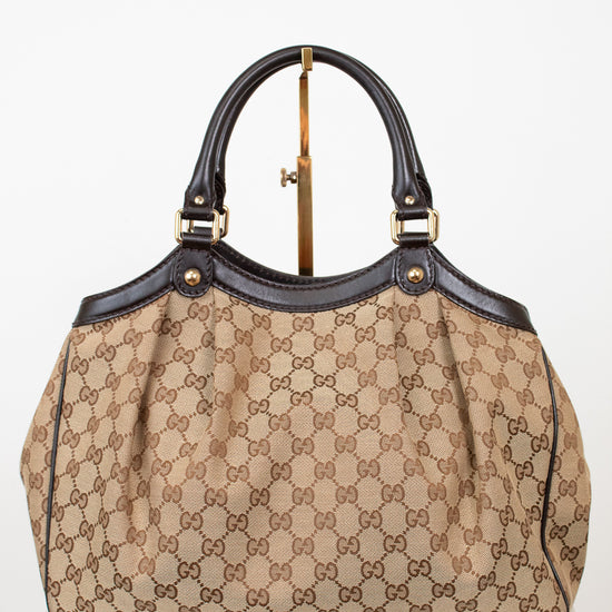 Beige handbag with brown Gucci monogram with brown handles on a white background