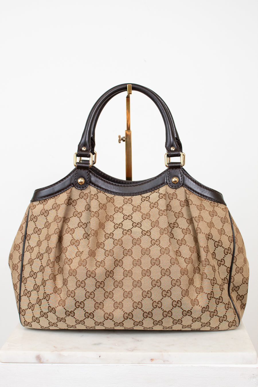 Beige handbag with brown Gucci monogram with brown handles on a white background