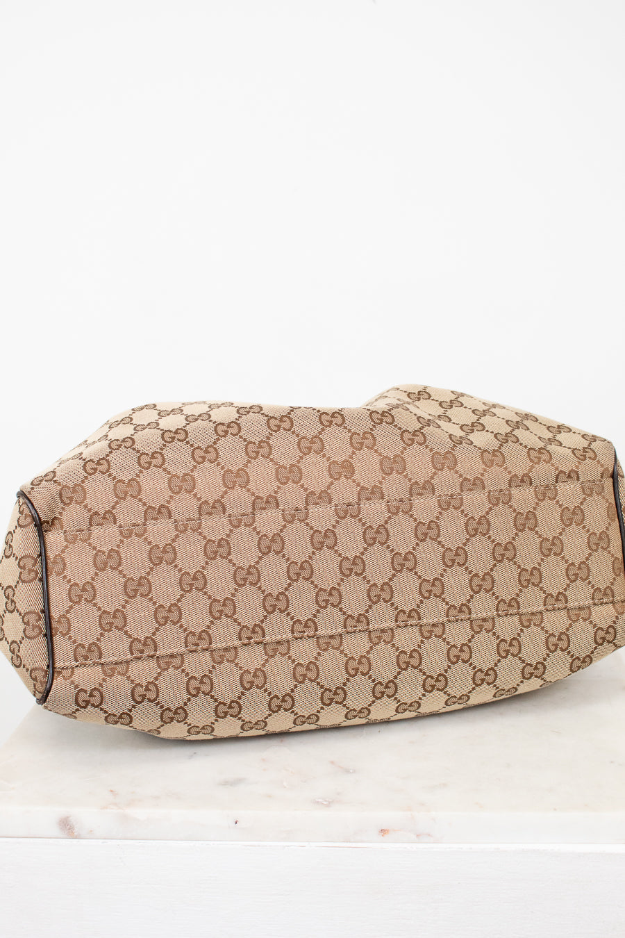Bottom view of beige handbag with Gucci monogram pattern on a white background