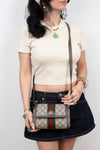A woman wearing a cream ribbed short-sleeve crop top and a dark denim mini skirt holds a Gucci GG Supreme crossbody bag with a brown leather strap against a plain white background.