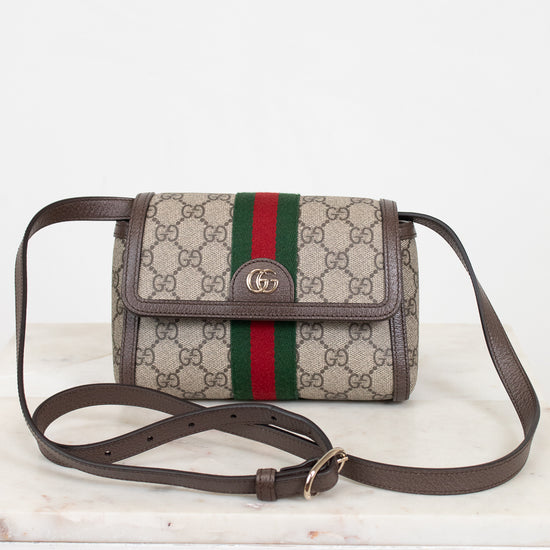 A Gucci monogram coated canvas crossbody bag with a brown leather strap and trim, featuring the signature green and red web stripe down the center and a gold-tone interlocking G logo on the front flap.