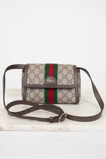 A Gucci monogram coated canvas crossbody bag with a brown leather strap and trim, featuring the signature green and red web stripe down the center and a gold-tone interlocking G logo on the front flap.