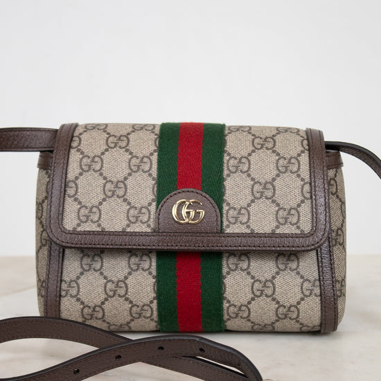 Gucci GG Supreme canvas shoulder bag with brown leather trim, a green and red web stripe, and a gold-tone GG logo on the front flap, shown with a adjustable brown strap on a light marble surface against a white background.
