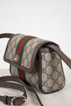 Gucci GG Supreme coated canvas shoulder bag with brown leather trim, a green and red web stripe, and gold-tone hardware, shown on a light marble surface against a white background.