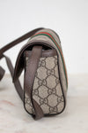 A close-up of the side view of a Gucci shoulder bag featuring the classic GG Supreme coated canvas in beige and brown, with dark brown leather trim and a signature green and red web stripe.