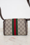 A small Gucci crossbody bag in beige GG Supreme coated canvas with brown leather trim and a signature green and red web stripe down the center, shown on a light marble surface against a white background.