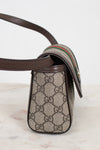 A close-up of a Gucci crossbody bag featuring the classic GG Supreme coated canvas in beige and brown, dark brown leather trim, and the signature green and red web stripe detail on the strap.