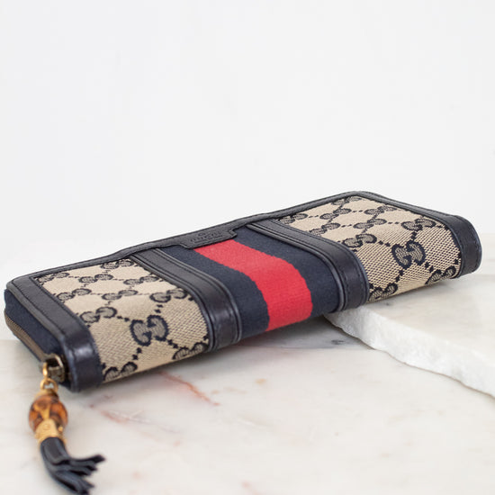 Navy and monogrammed zip around wallet with red and navy striped center detail with gold and bamboo zipper laying flat on marble background showing bottom edge details