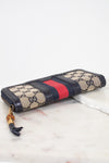Navy and monogrammed zip around wallet with red and navy striped center detail with gold and bamboo zipper laying flat on marble background showing bottom edge details
