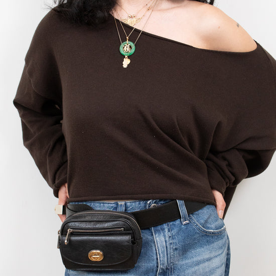 Person wearing a brown off-shoulder top and blue jeans with a black belt bag on a white background