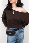 Person wearing a brown off-shoulder top and blue jeans with a black belt bag on a white background