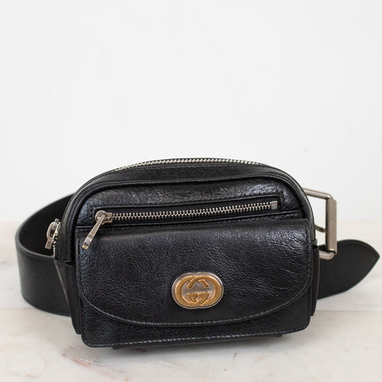 Black leather belt bag with gold logo on a light marble background