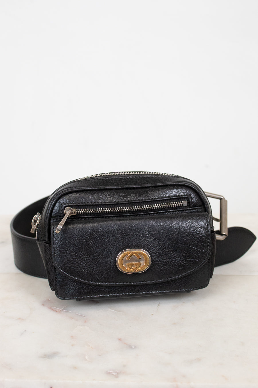 Black leather belt bag with gold logo on a light marble background