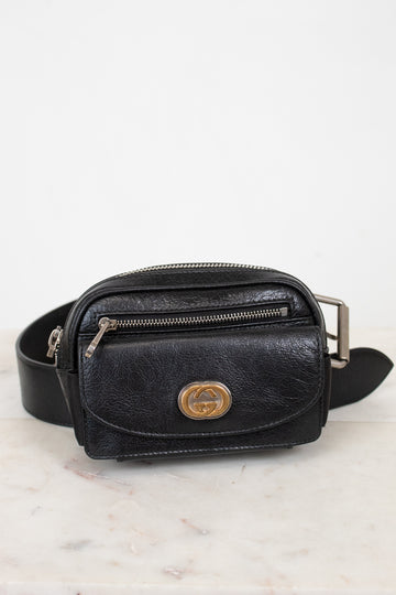 Black leather belt bag with gold logo on a light marble background
