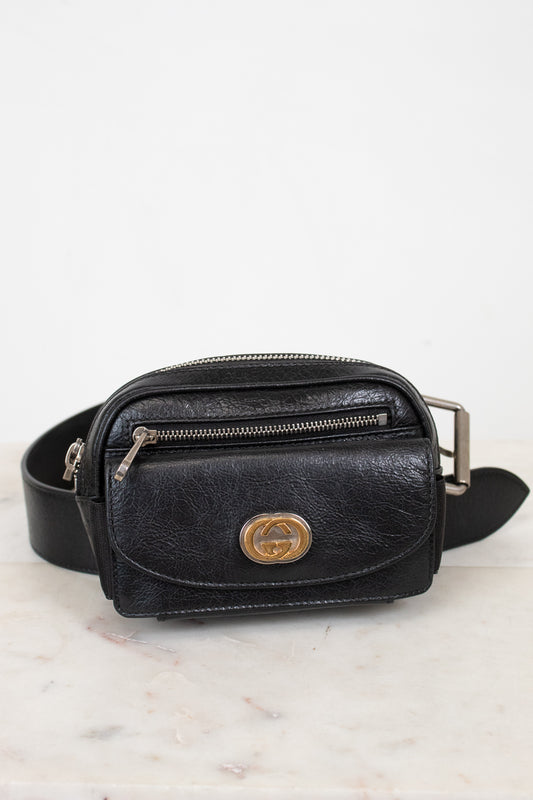 Black leather belt bag with gold logo on a light marble background