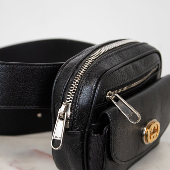 Black leather belt bag with gold clasp on a marble surface