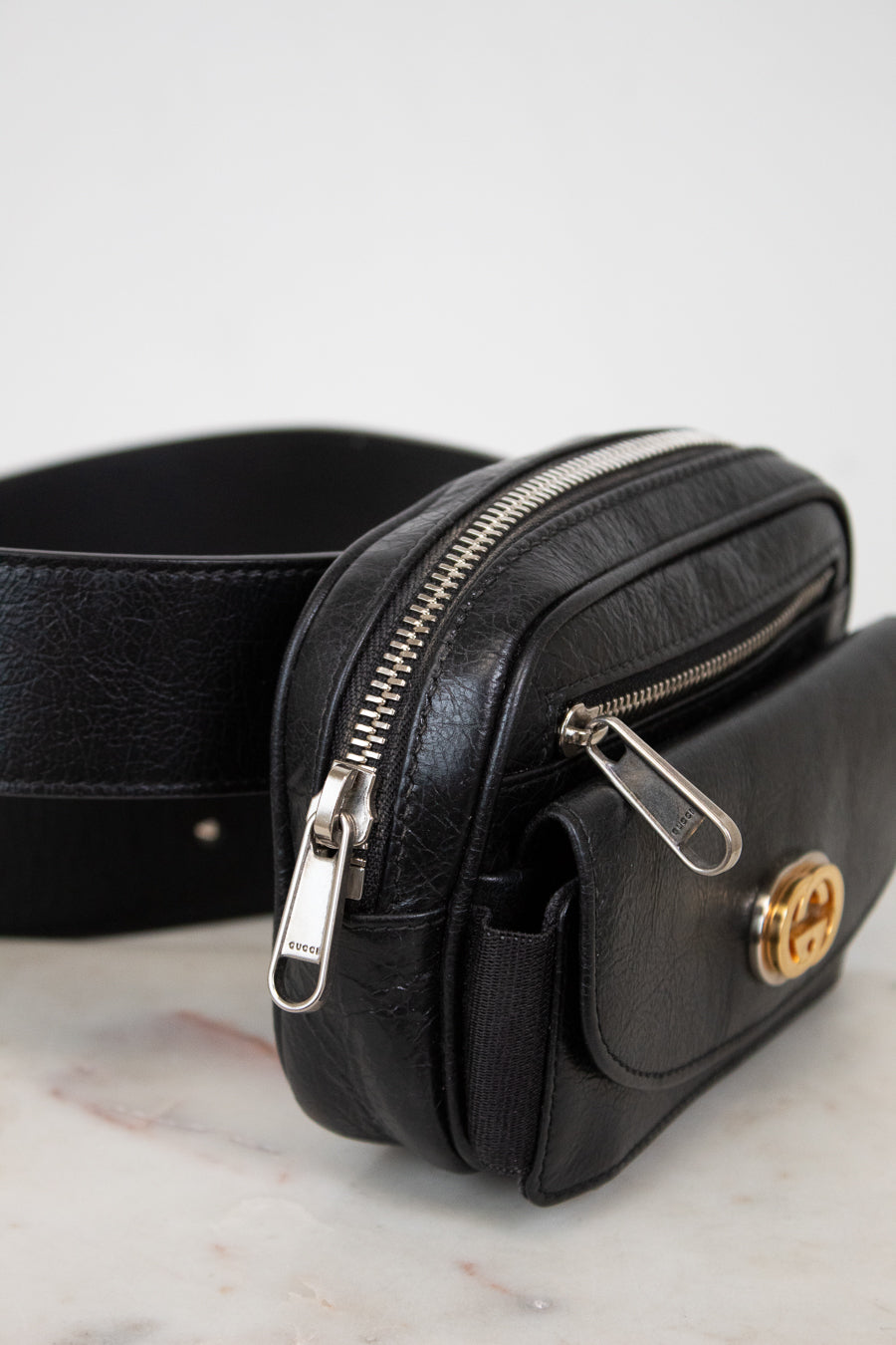 Black leather belt bag with gold clasp on a marble surface