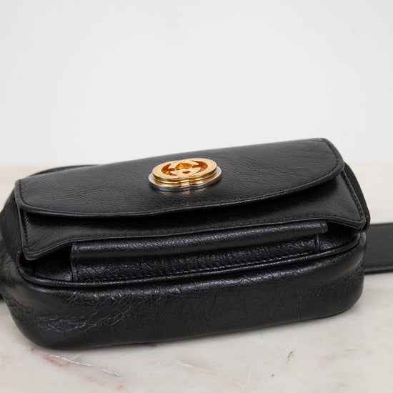 Black leather belt bag with gold clasp on a marble surface