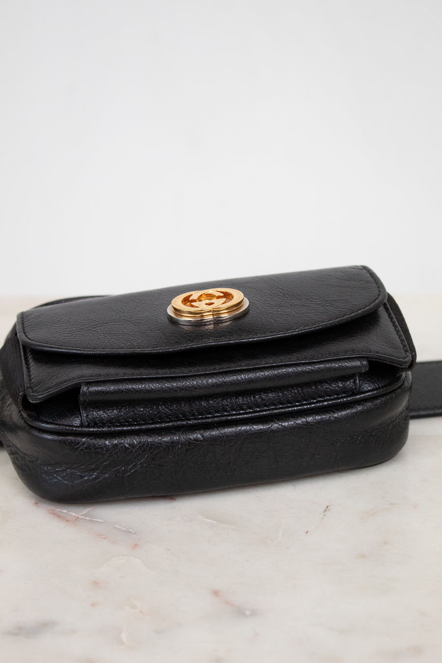 Black leather belt bag with gold clasp on a marble surface