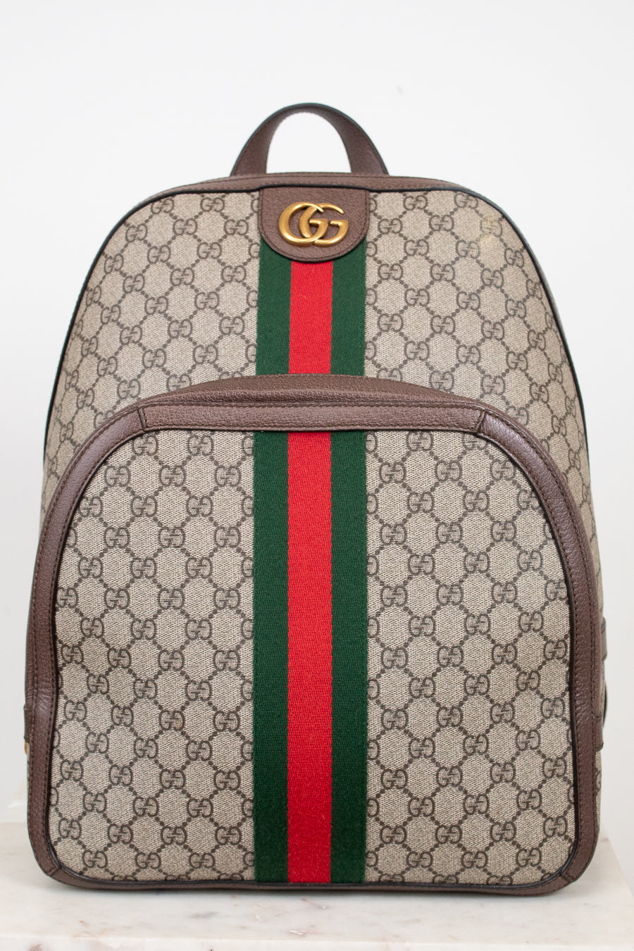 Gucci GG Supreme coated canvas backpack with brown leather trim, a green and red web stripe down the center, and a gold-tone GG logo on the front.
