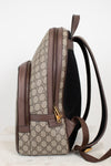 A Gucci backpack shown from the side, featuring the brand's signature GG Supreme coated canvas in beige and brown, brown leather trim, a black mesh back panel, and gold-tone hardware.