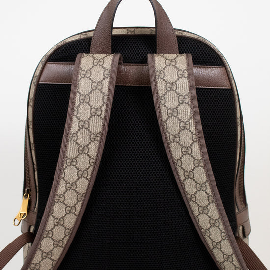 The back view of a Gucci backpack featuring a black mesh back panel, brown leather trim, and beige and brown GG monogram coated canvas shoulder straps.