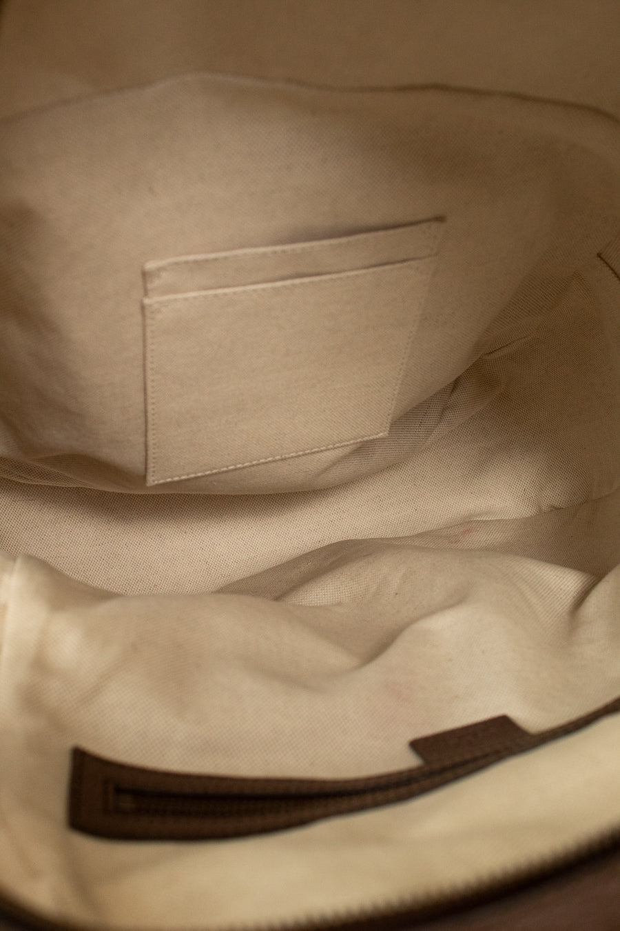 Close-up of the interior beige lining of a Gucci GG Supreme coated canvas backpack, showing a stitched interior pocket and a dark brown zipper track.