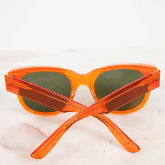 Orange translucent acetate sunglasses with dark lenses, resting on a light marble surface against a white background.
