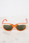 Orange acetate sunglasses with cream details and dark lenses resting on a white marble surface against a white background.