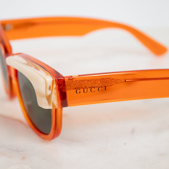Close-up of Gucci sunglasses with translucent orange acetate frames and dark lenses, resting on a light marble surface.