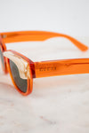 Close-up of Gucci sunglasses with translucent orange acetate frames and dark lenses, resting on a light marble surface.