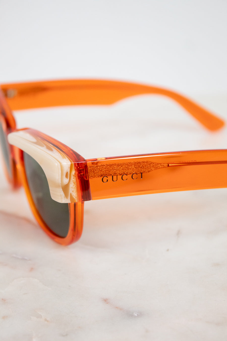 Close-up of Gucci sunglasses with translucent orange acetate frames and dark lenses, resting on a light marble surface.