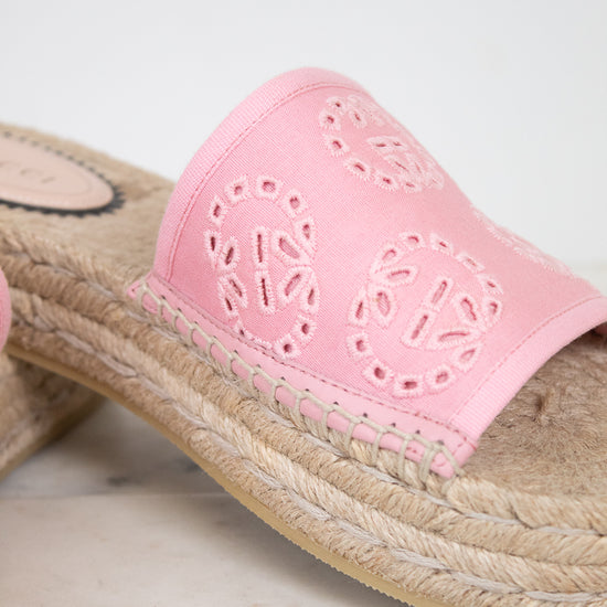 A close-up of a pink espadrille slide sandal with a woven jute platform sole and a pink leather upper featuring circular cutout patterns.