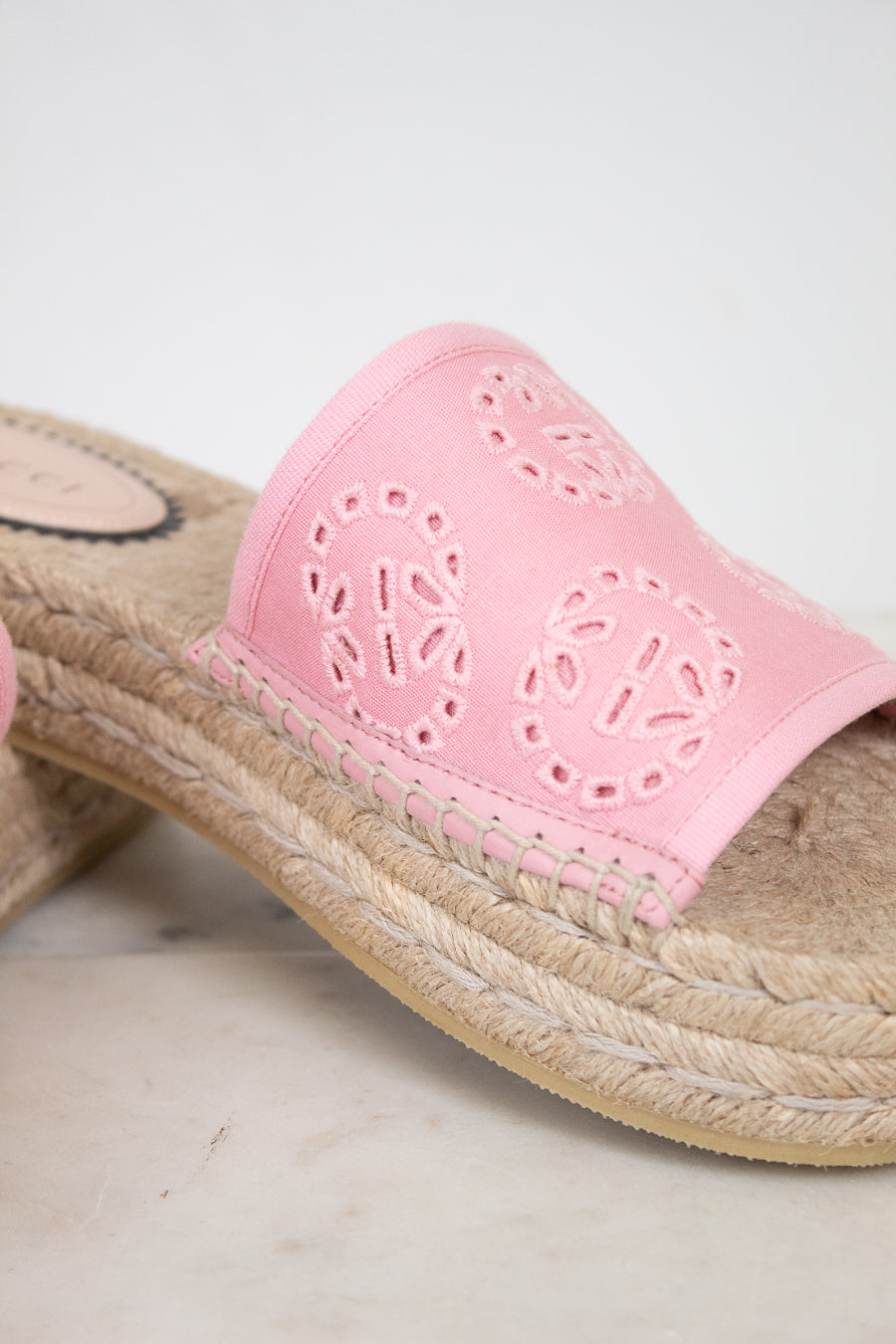 A close-up of a pink espadrille slide sandal with a woven jute platform sole and a pink leather upper featuring circular cutout patterns.