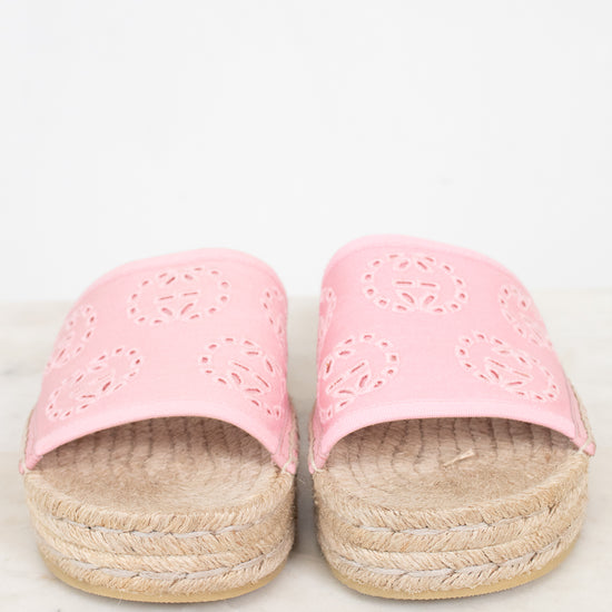 A pair of pink espadrille slide sandals with laser-cut circular patterns on the straps and braided jute platform soles, shown on a light marble surface against a white background.