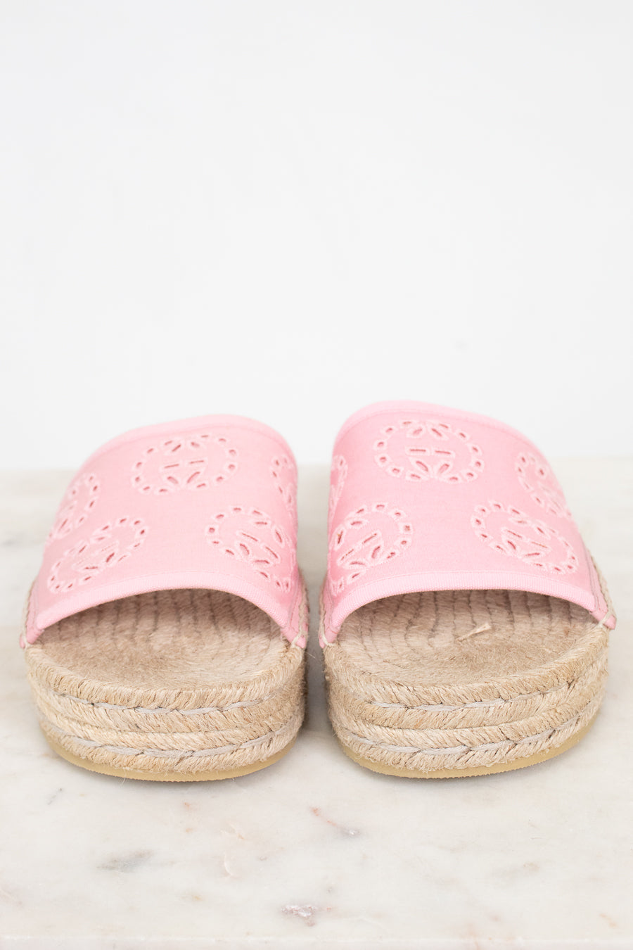 A pair of pink espadrille slide sandals with laser-cut circular patterns on the straps and braided jute platform soles, shown on a light marble surface against a white background.