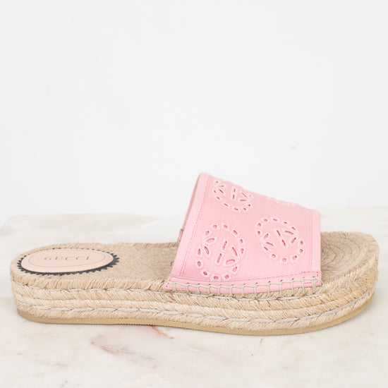 A single pink espadrille slide sandal with laser-cut circular patterns on the strap, resting on a light marble surface against a white background.