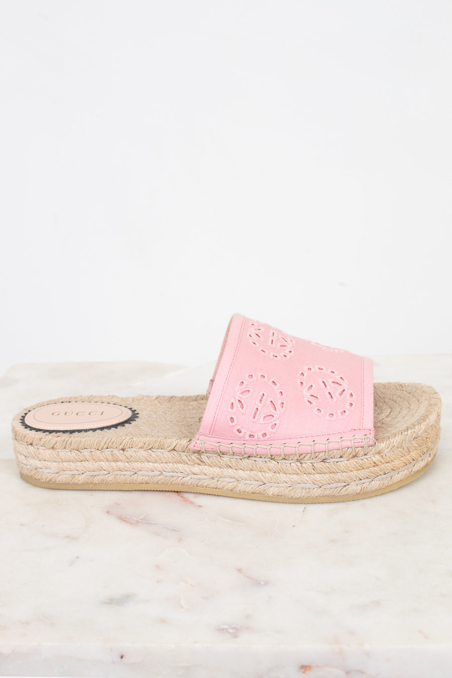 A single pink espadrille slide sandal with laser-cut circular patterns on the strap, resting on a light marble surface against a white background.