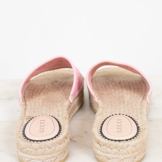 A pair of Gucci espadrille sandals with pink straps and natural jute-wrapped soles, photographed from the back on a light marble surface.